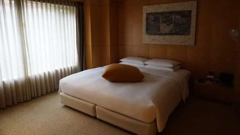 Minimalist guest room at Grand Hyatt Fukuoka featuring soft natural light, layered bedding, and serene wood-accented walls.