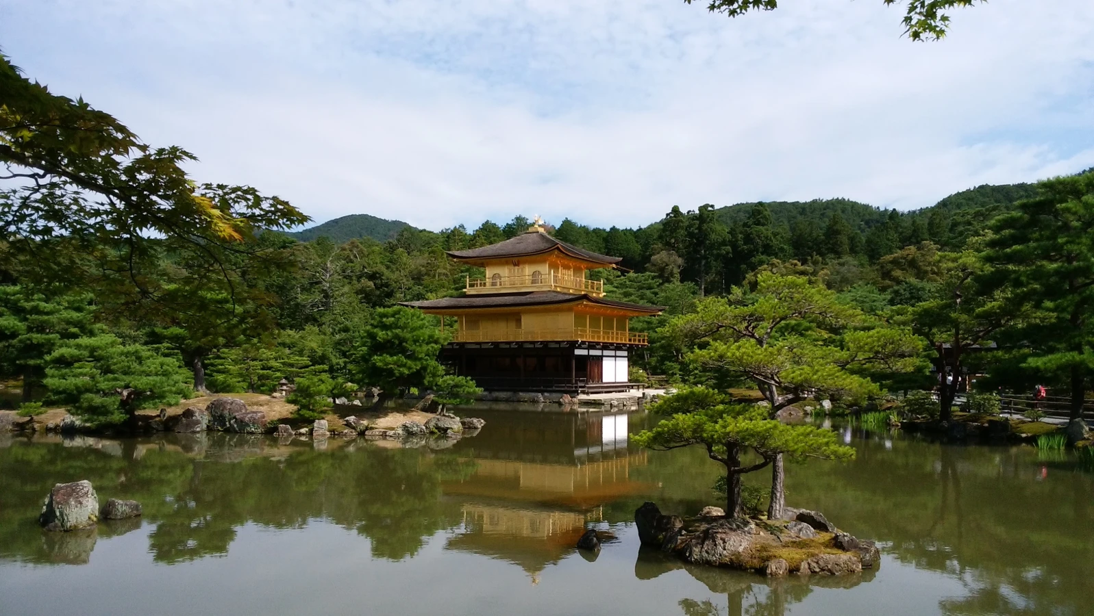 Golden Pavilion at Kinkakuji Temple reflected in the still waters of Kyoko-chi pond, framed by pines and distant hills in Kyoto.