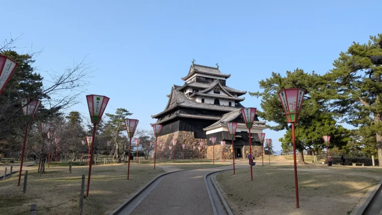 Matsue Castle in Chugoku, viewed from a lantern-lined path during early spring, showcasing the historic black-walled keep under clear skies.