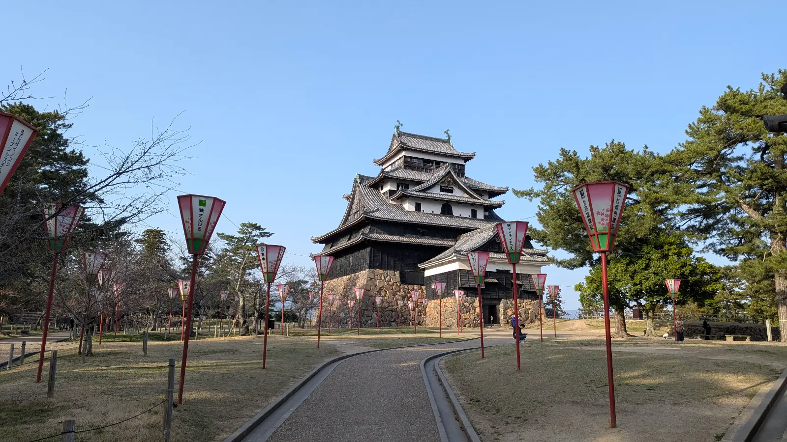 Matsue Castle in Chugoku, viewed from a lantern-lined path during early spring, showcasing the historic black-walled keep under clear skies.