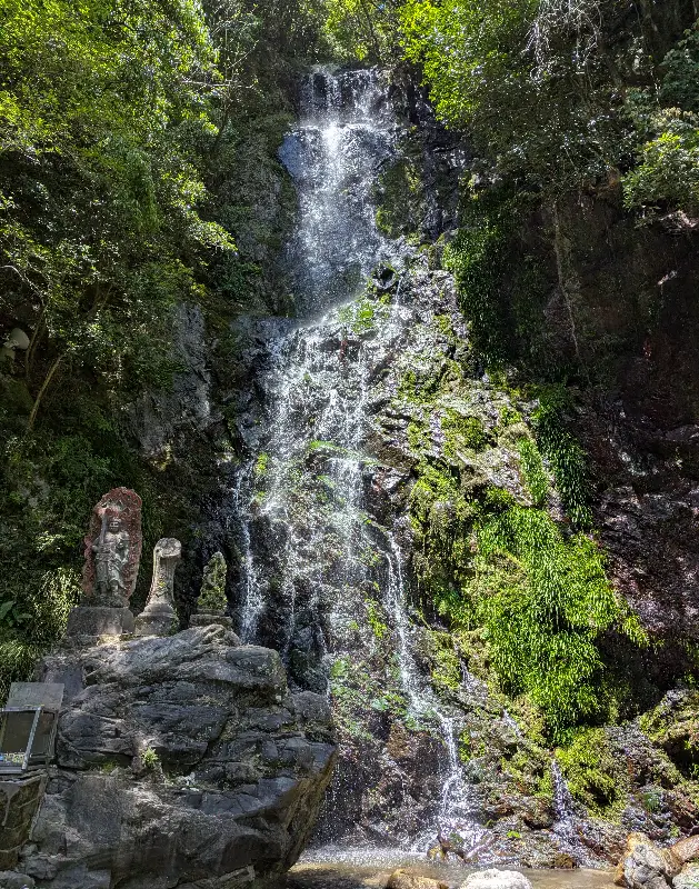 Kiyomizu Waterfall cascading down a mossy cliffside in Ogi, Saga Prefecture, with guardian statues at its base.