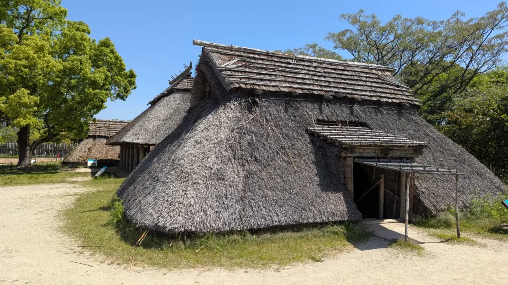 Thatched-roof Yayoi-era house under blue sky at Yoshinogari Historical Park, capturing the stillness of early Japanese settlement in Saga.