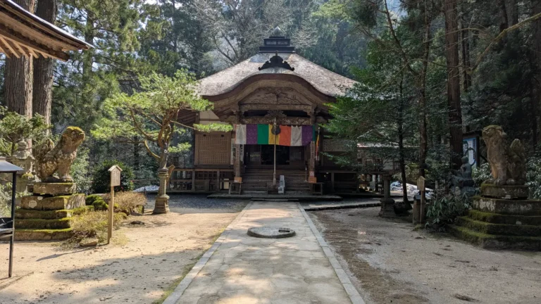 Main hall of Sanbutsu-ji Temple in Tottori, Japan, framed by tall cedars and stone guardians at the forested base of Mount Mitoku.