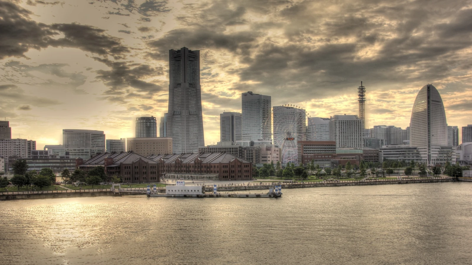 Yokohama’s skyline and Red Brick Warehouses at dusk, seen across the water under a dramatic sky.